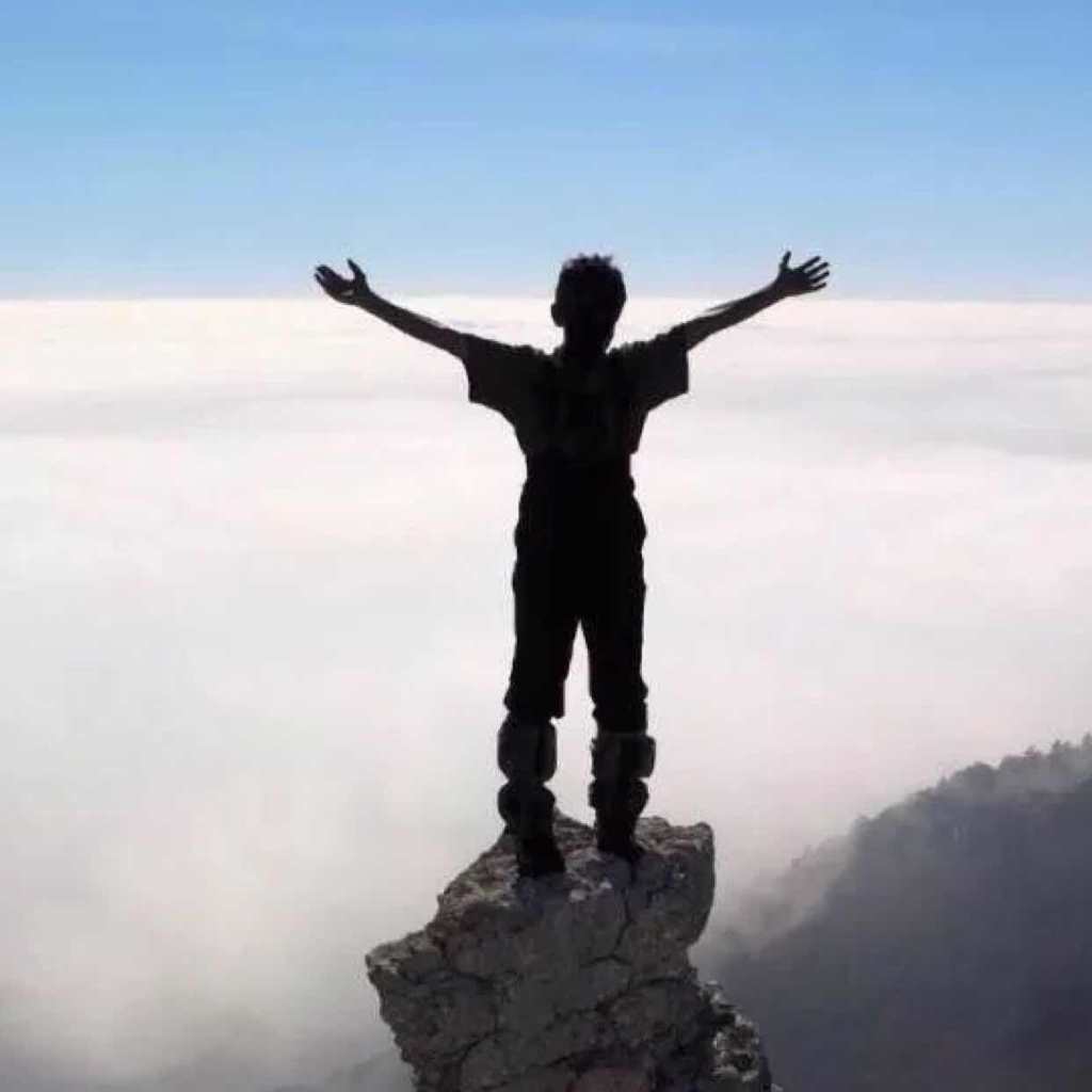 一个人张开双手站在山顶上的岩石上的照片